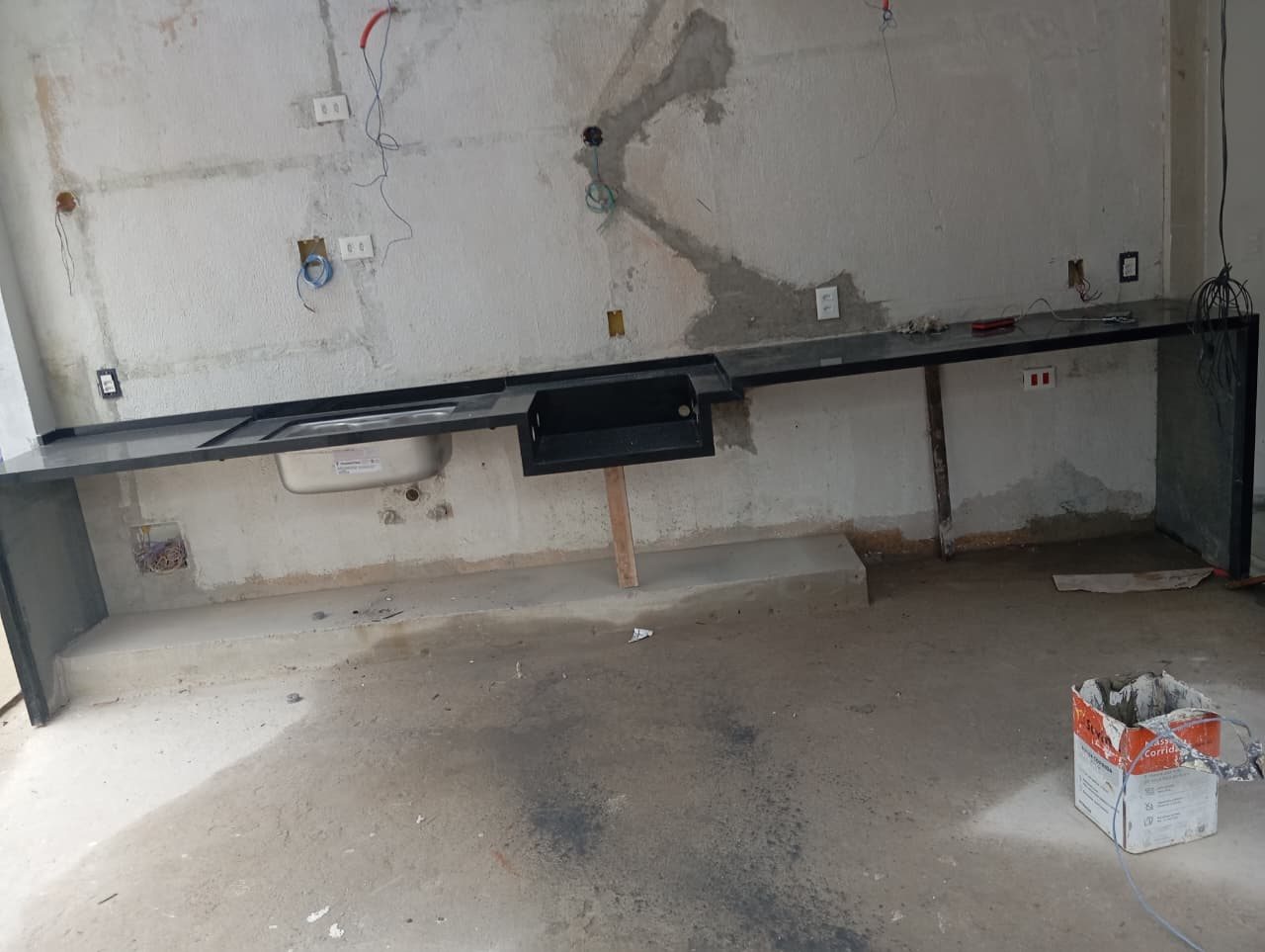 Vista ampla da bancada preta com pia e churrasqueira em instalação