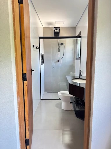 Banheiro do Palulu Flat com box de vidro, bancada e revestimentos claros
