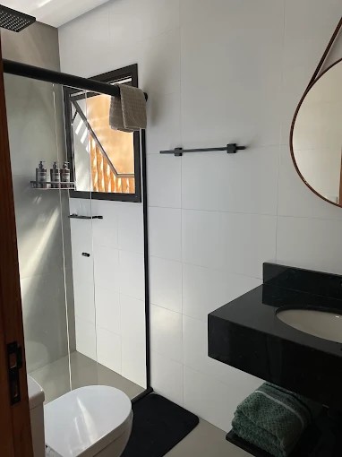 Outro banheiro do Palulu Flat com box de vidro, bancada preta e revestimento claro