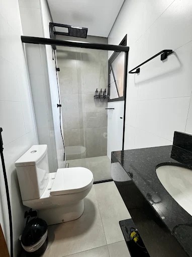 Banheiro do Palulu Flat com bancada preta, vaso sanitário e box com perfis escuros
