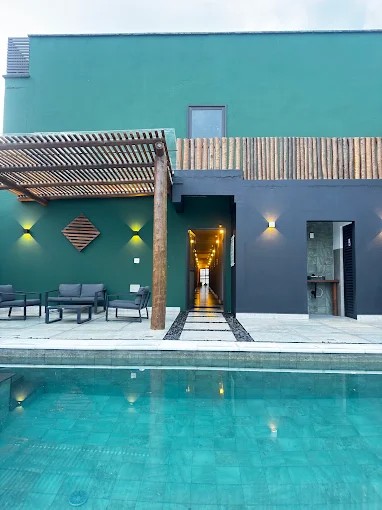 Piscina do Palulu Flat com fachada da área de lazer e pergolado de madeira