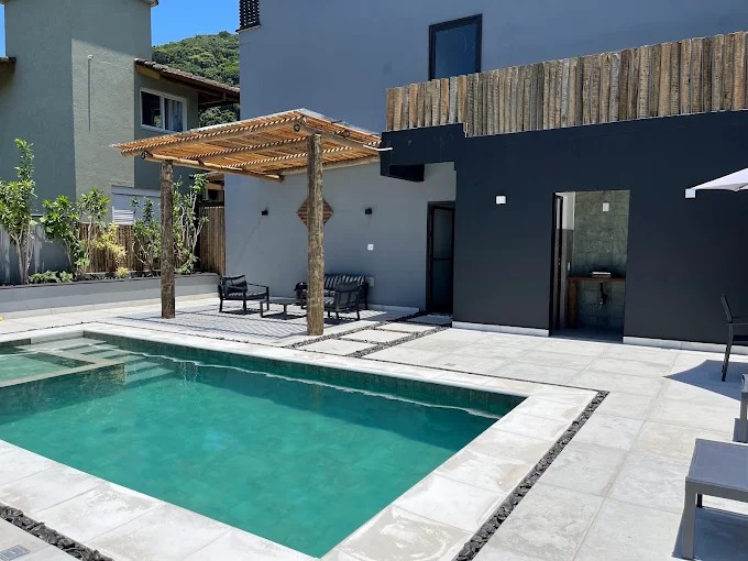 Piscina do Palulu Flat com bordas claras, pergolado e volumes da edificação ao fundo