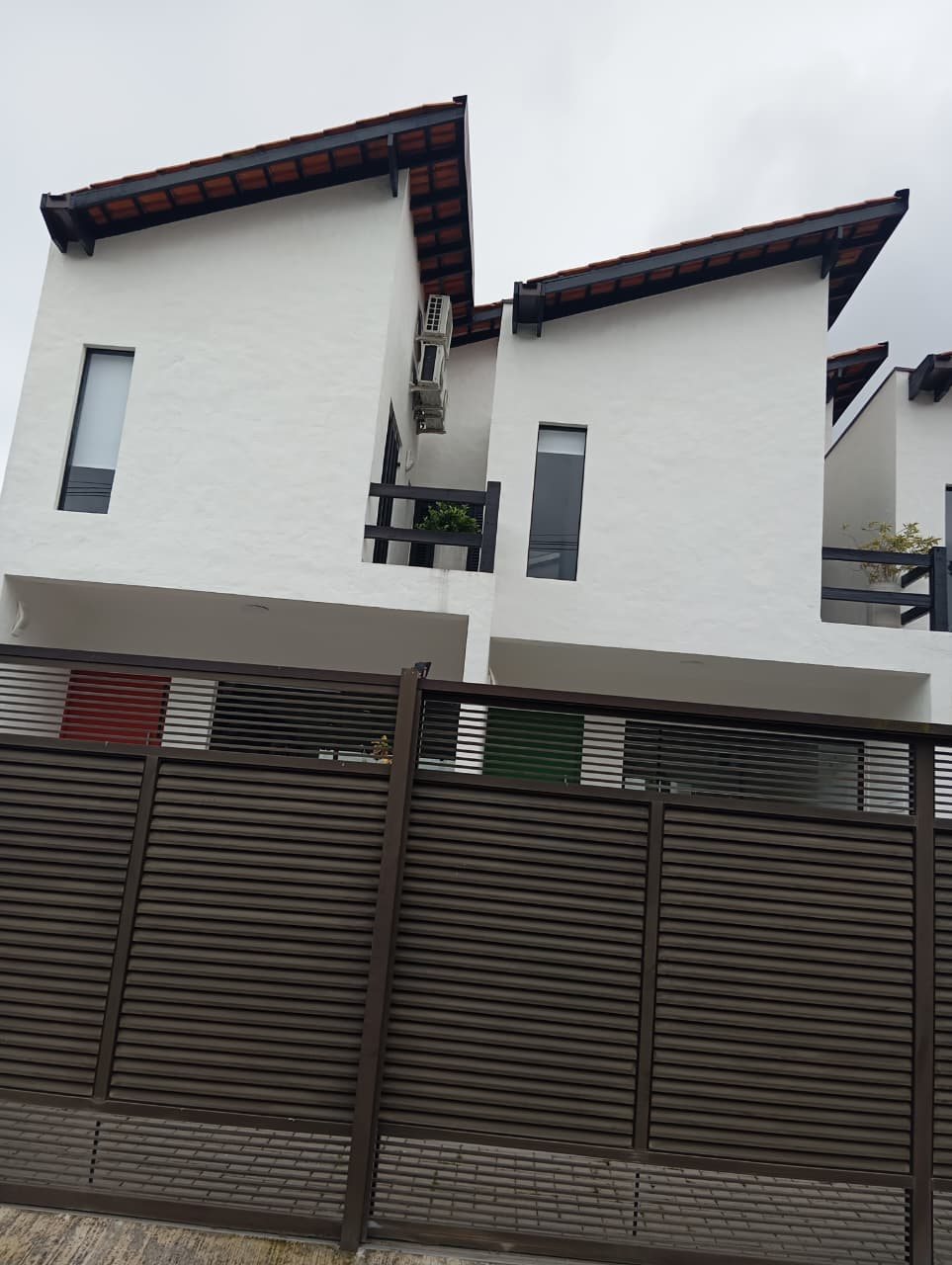 Outro ângulo dos volumes brancos, coberturas e portões do conjunto de três casas